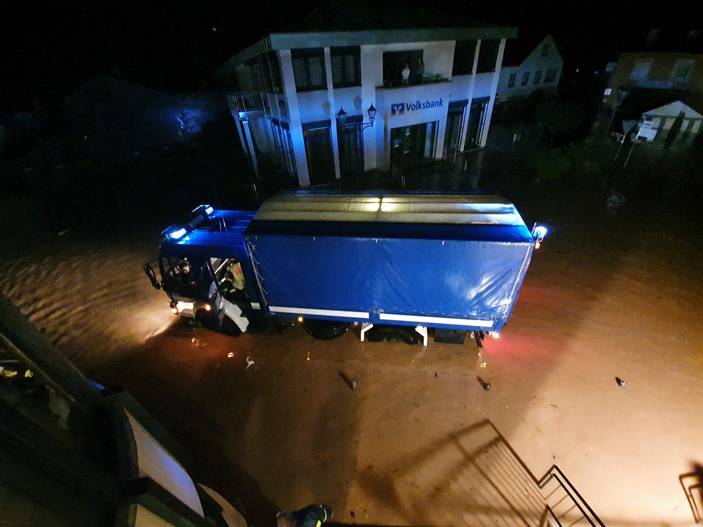 THW-Lastwagen der Fachgruppe Notversorgung steht nachts im Hochwasser vor einem überfluteten Gebäude