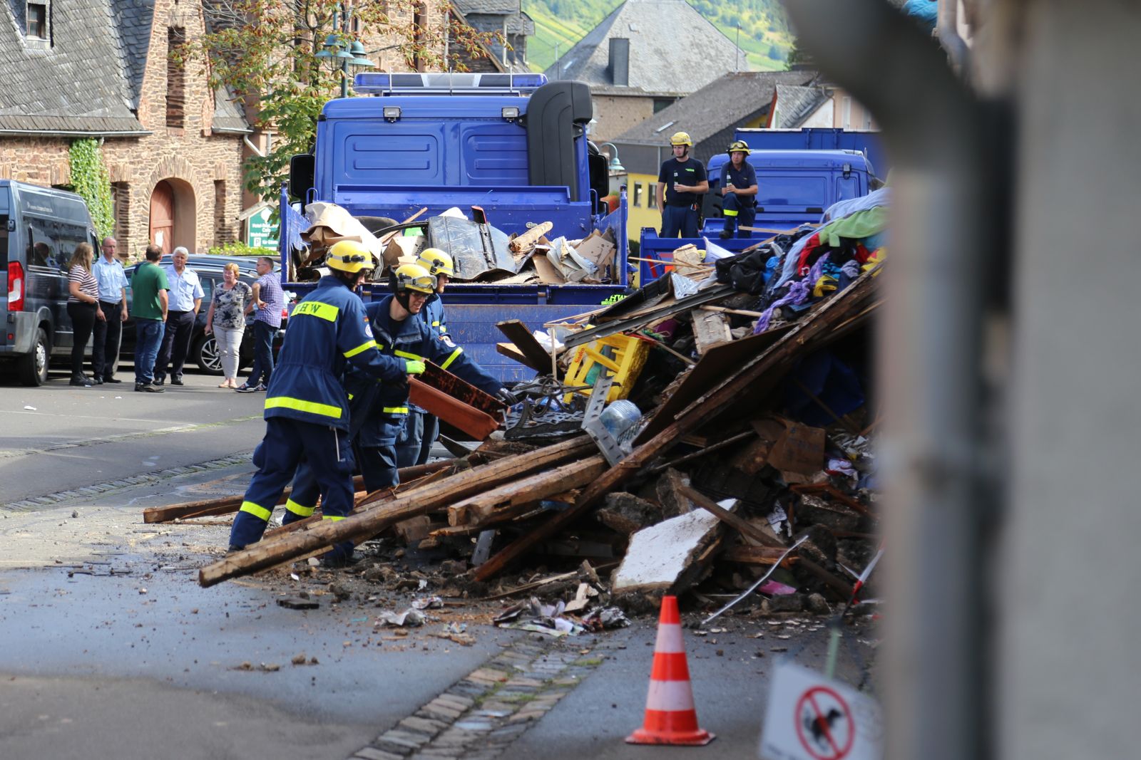 THW-Helfer räumen Holz und Trümmer eines teilweise abgerissenen Gebäudes auf die Ladefläche eines Kippers